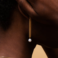 Load image into Gallery viewer, Gold earring with a long bar and a round pearl worn by model
